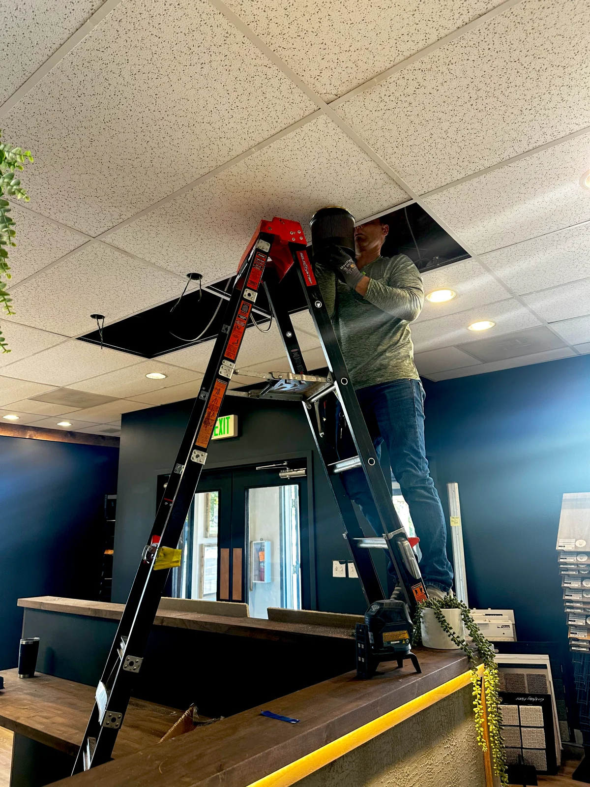 Electrician on a ladder working above a drop ceiling in a retail space
