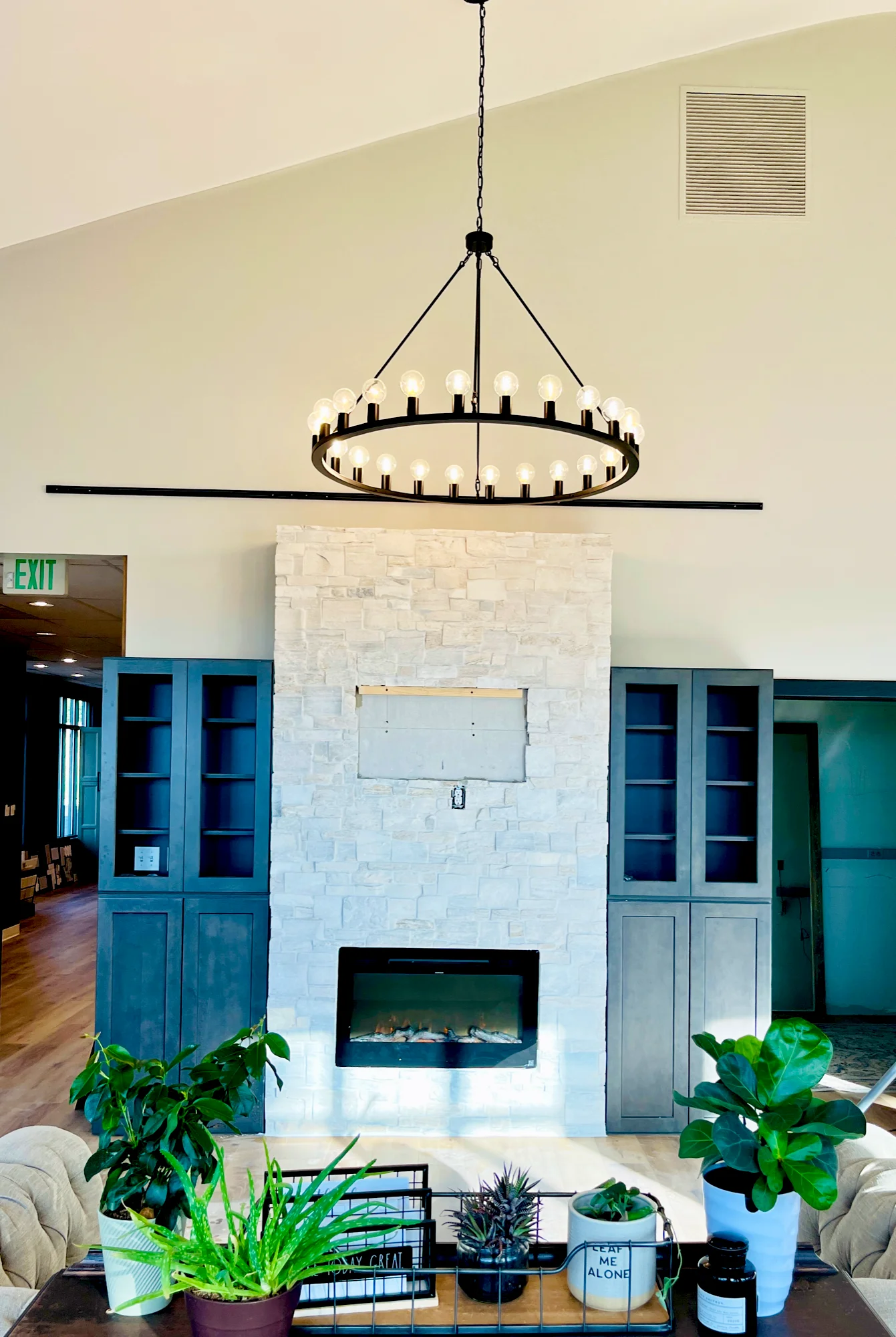 Ring chandelier hung from a vaulted ceiling above a stone fireplace with built-in shelving