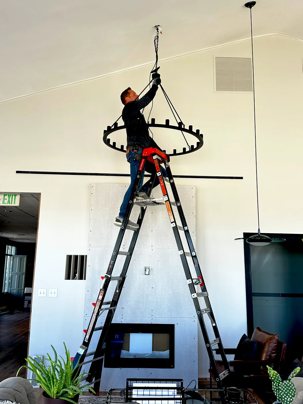 Electrician on a tall ladder lifting a ring chandelier to the ceiling