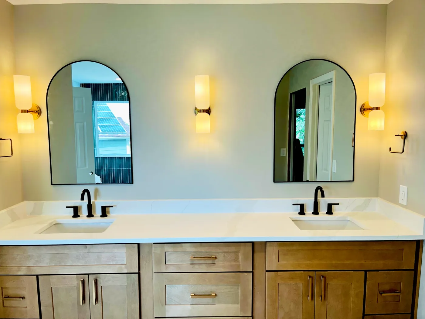 Double vanity with arched mirrors and brass sconces