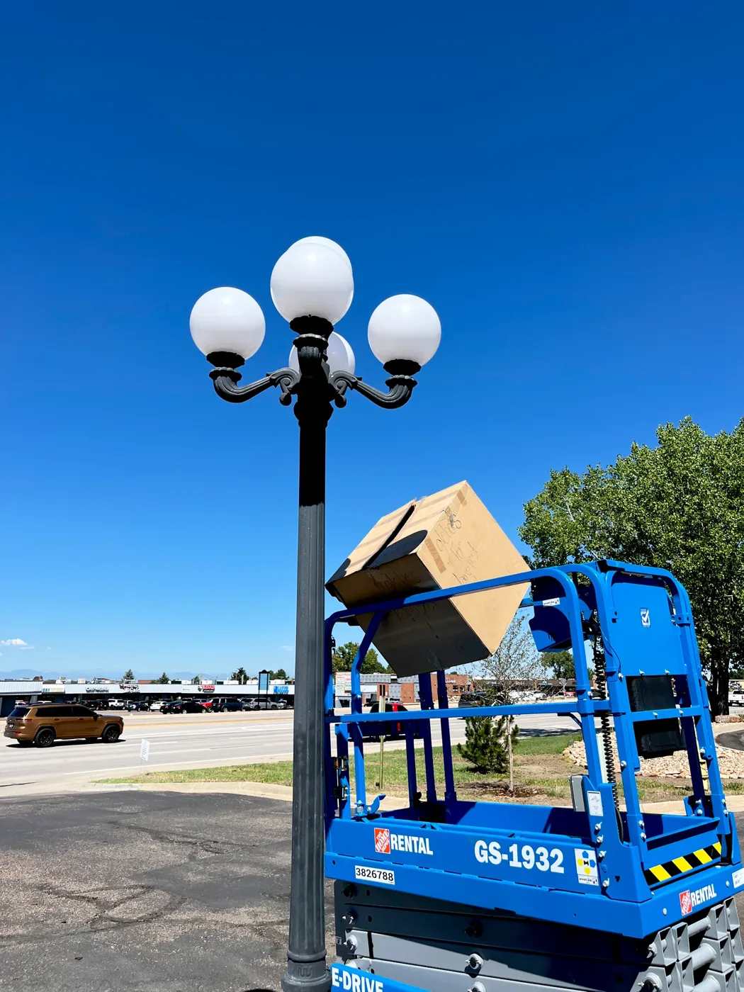 Electrician on a scissor lift setting globes on a parking lot light pole