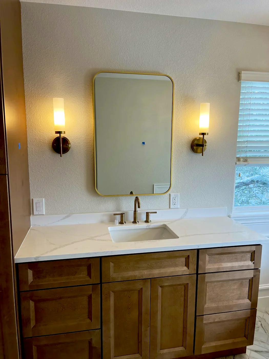 Bathroom vanity with brass sconces and a gold-framed mirror